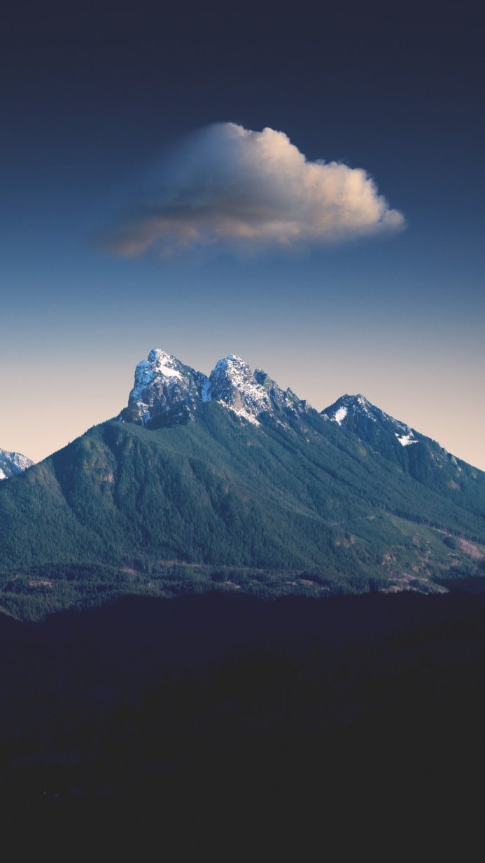 A mountain range with snow-capped peaks and a single cloud floating above it