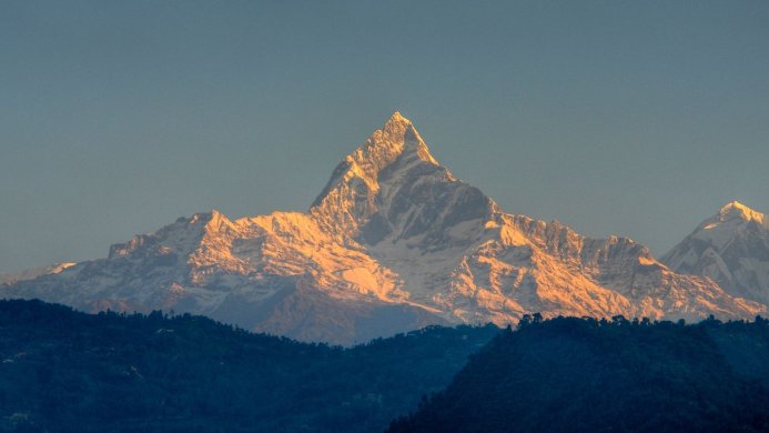 Snow-capped mountain peak at sunrise with blue sky and green foothills