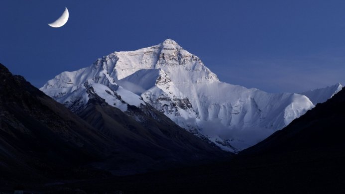 Snowy mountain under a crescent moon against a dark blue sky