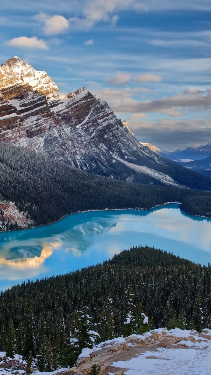 Snowy mountain overlooking a turquoise lake surrounded by evergreen trees