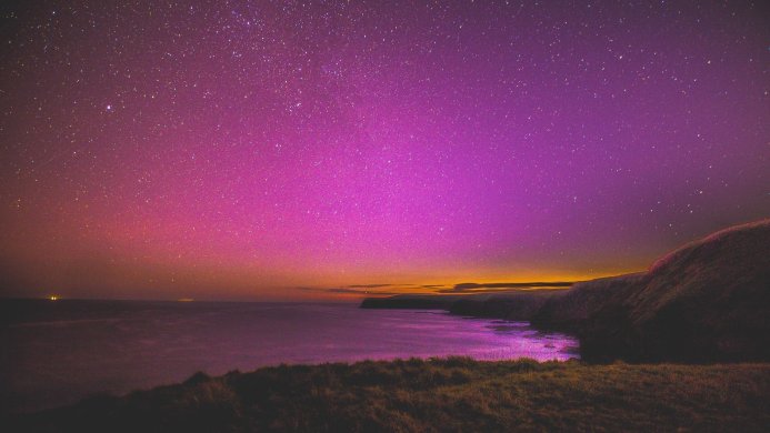Starry night sky over the sea and coastline with vivid purple, pink, and orange colors