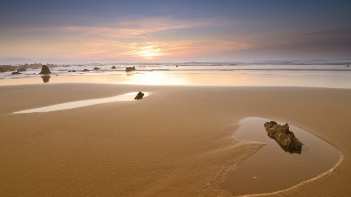 Golden sunset over a sandy beach with rock formations and the sea reflecting the light