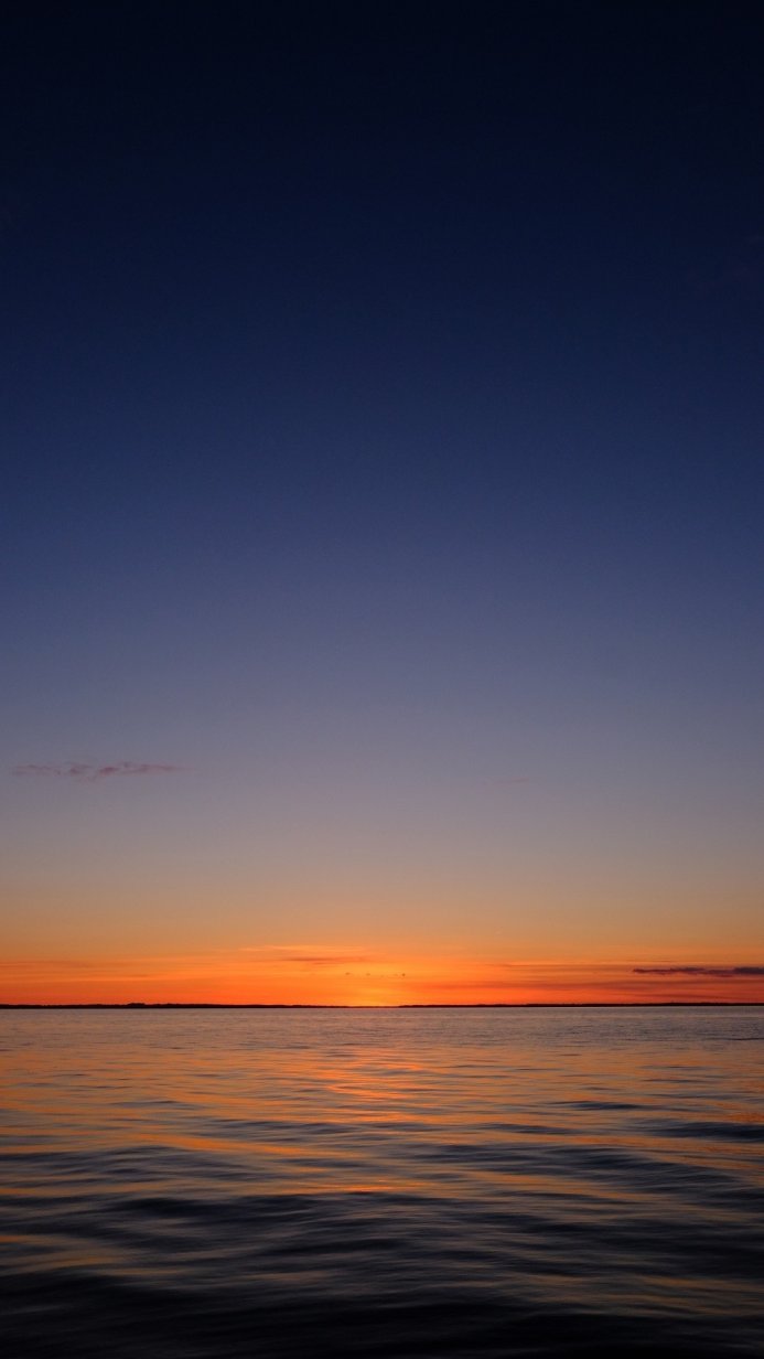 Sunset over water, transitioning from orange to blue sky