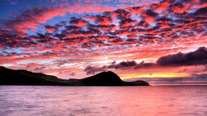 Beautiful sunset over the sea with red clouds and a mountain on the horizon