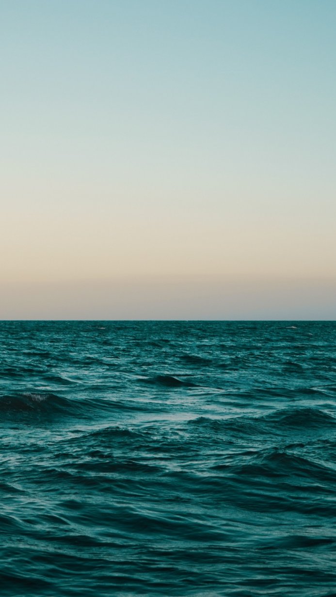Calm teal ocean with waves under a gradient blue and yellow sky