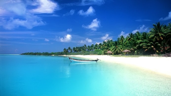A boat sits on a white sand beach surrounded by turquoise water and palm trees under a blue sky