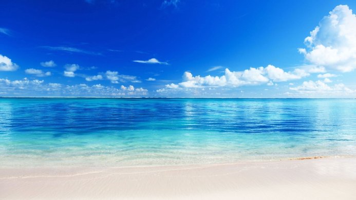 Beautiful seascape with clear blue water, white sand, and fluffy clouds in a bright blue sky