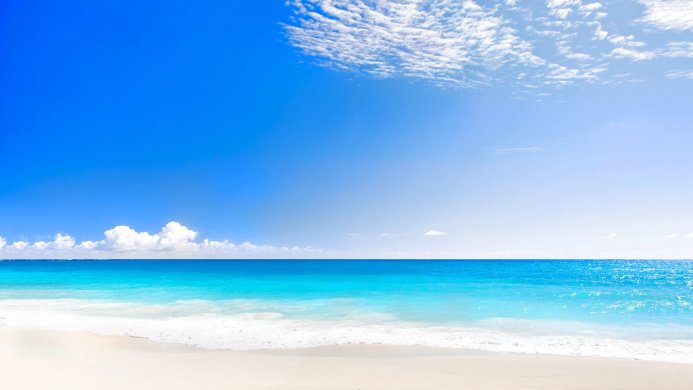 Blue sea meets a clear sky at a sandy beach, with fluffy white clouds above