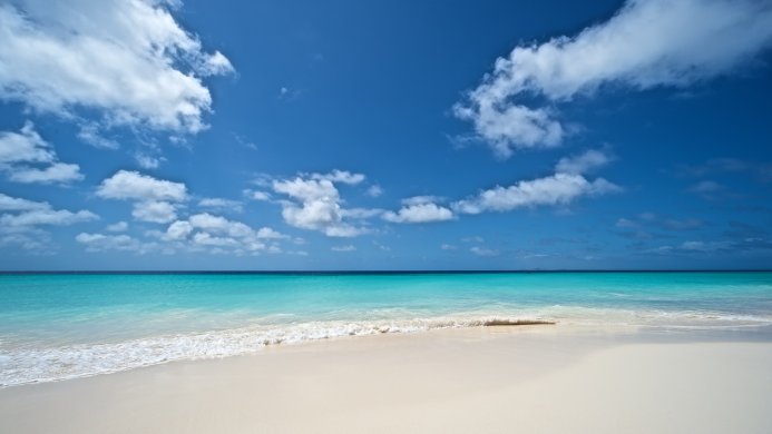 Beautiful beach with turquoise water and white sand under a blue sky with clouds