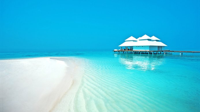 White house on stilts over turquoise water in a tropical paradise with a white sand beach