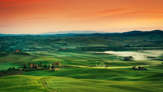 Tuscan landscape with rolling green hills and houses at sunset