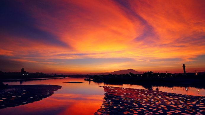 Sunset over water reflecting the sky's vibrant colors with a city skyline in the distance