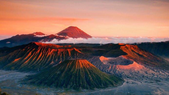 Aerial view of a volcano surrounded by mountains with an orange sky at sunrise