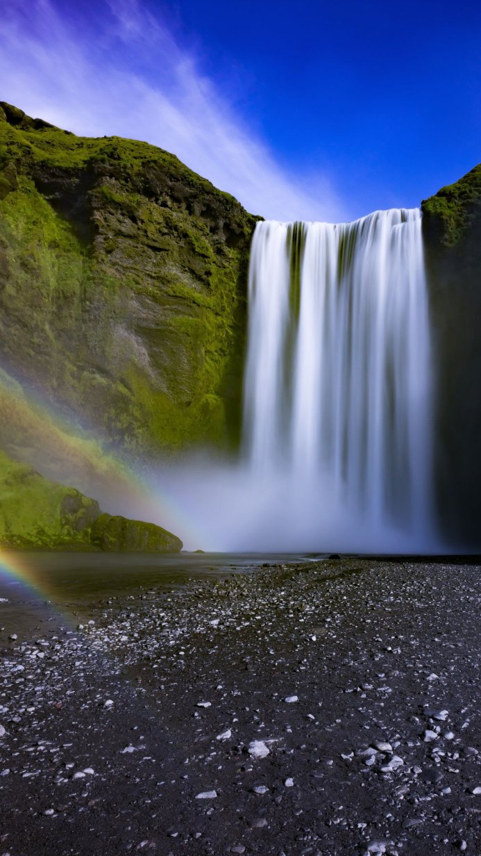 A majestic waterfall cascading down a moss-covered cliff with a vibrant rainbow at its base