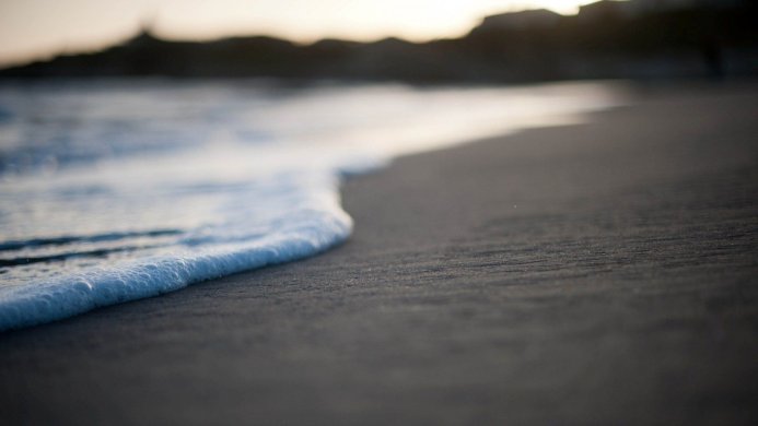 Waves gently washing up on a dark sand beach, early morning light