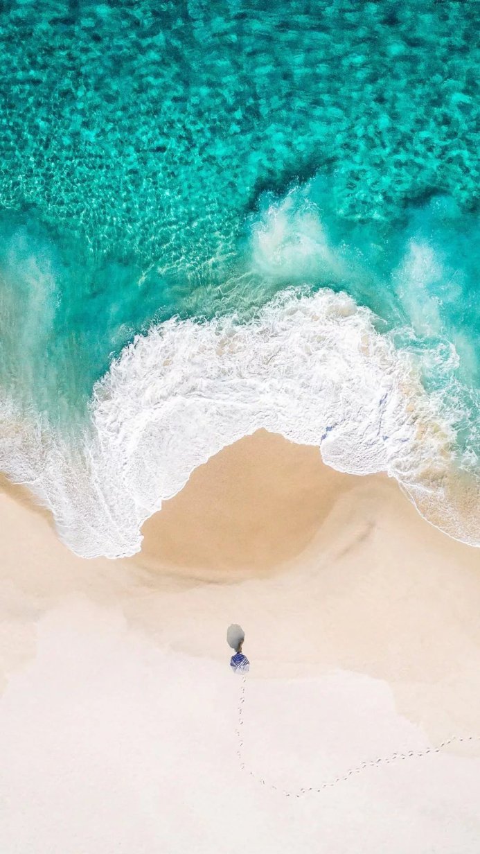 Aerial view of a beach with turquoise water, white sand and a small umbrella