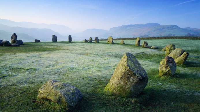 Castlerigg Stone Circle in the Lake District, with a field of grass, mountains, and a clear sky