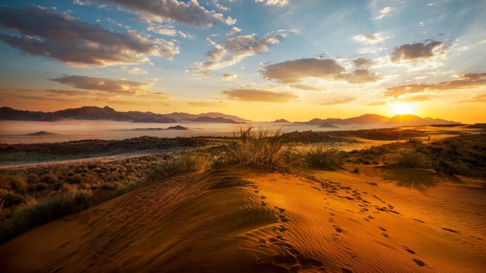Sunrise over a desert landscape with sand dunes and distant mountains