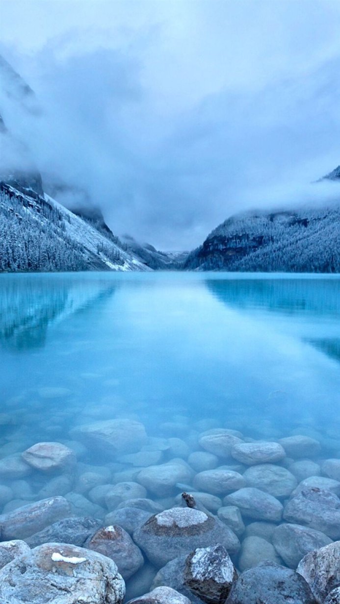 A serene mountain lake with snowy mountains and visible rocks underwater