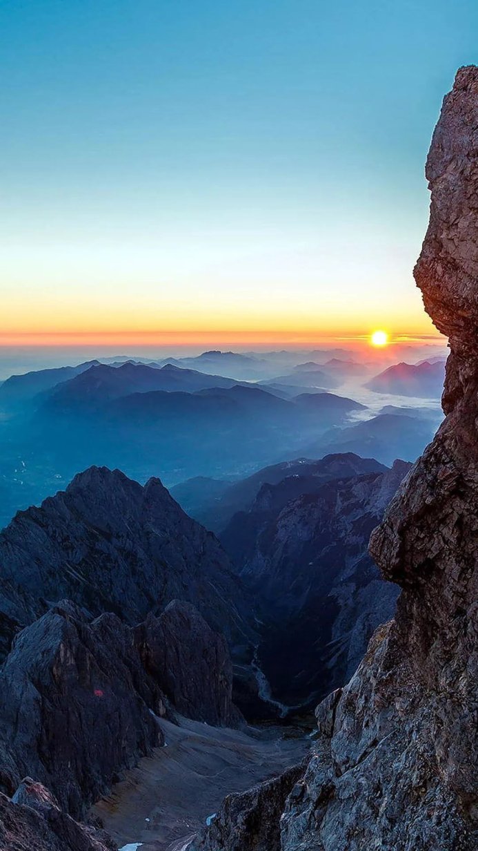 Mountain range at sunrise with blue and orange hues and a large rock in the foreground
