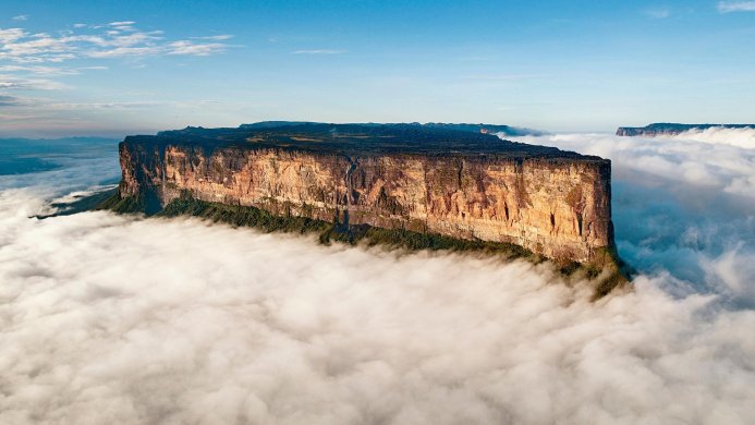 Aerial view of a table mountain surrounded by clouds with a blue sky above