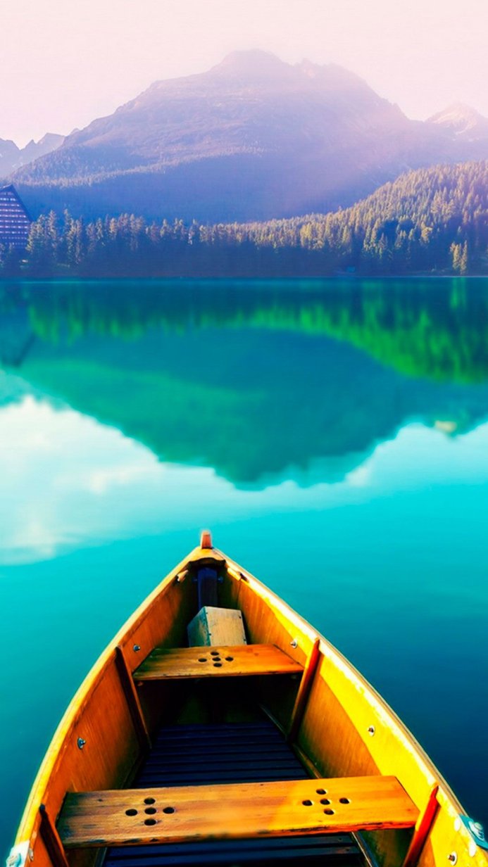 A wooden boat floating on a still lake with mountains in the background
