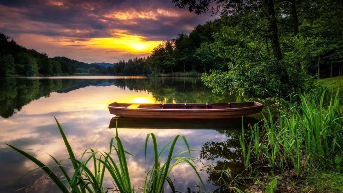 A wooden boat on a calm lake during sunset reflecting sky and trees