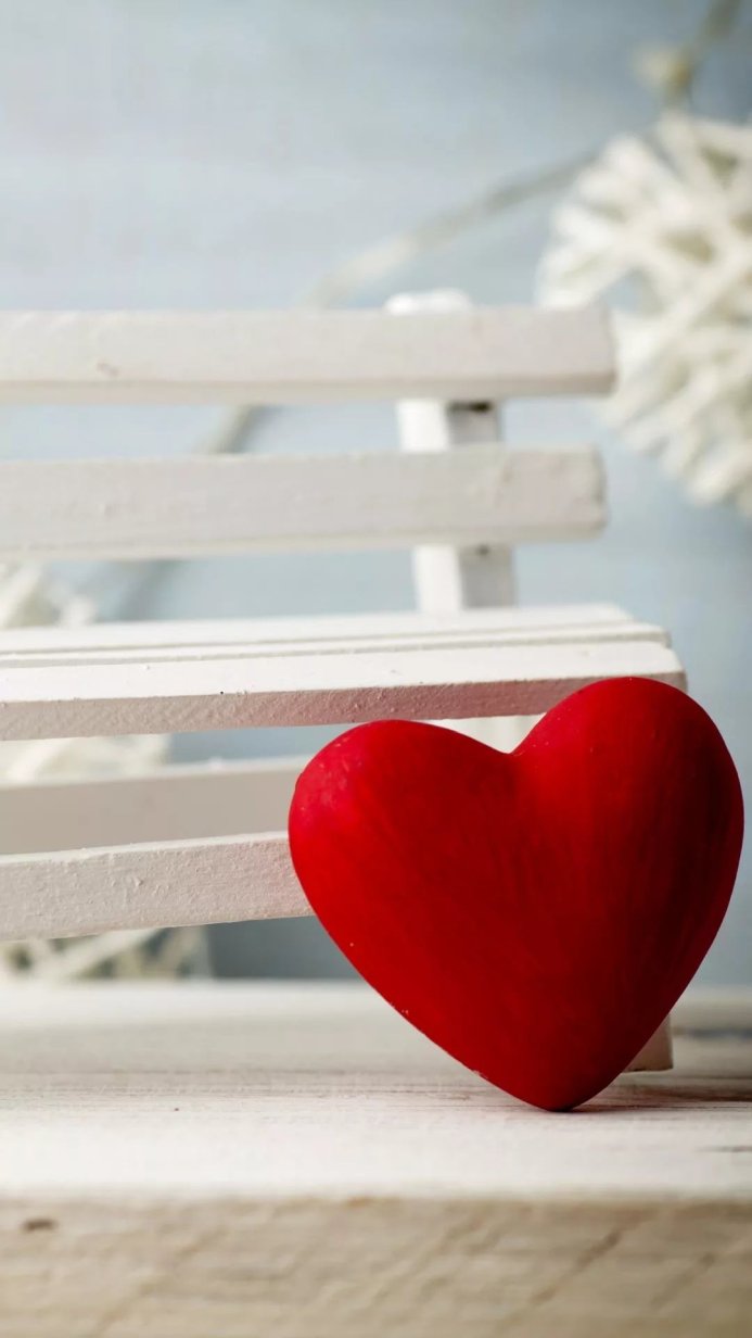 Red heart leaning against a white wooden bench
