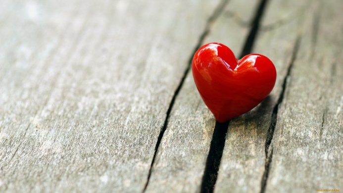 A red heart on a rustic wooden surface with visible cracks and texture