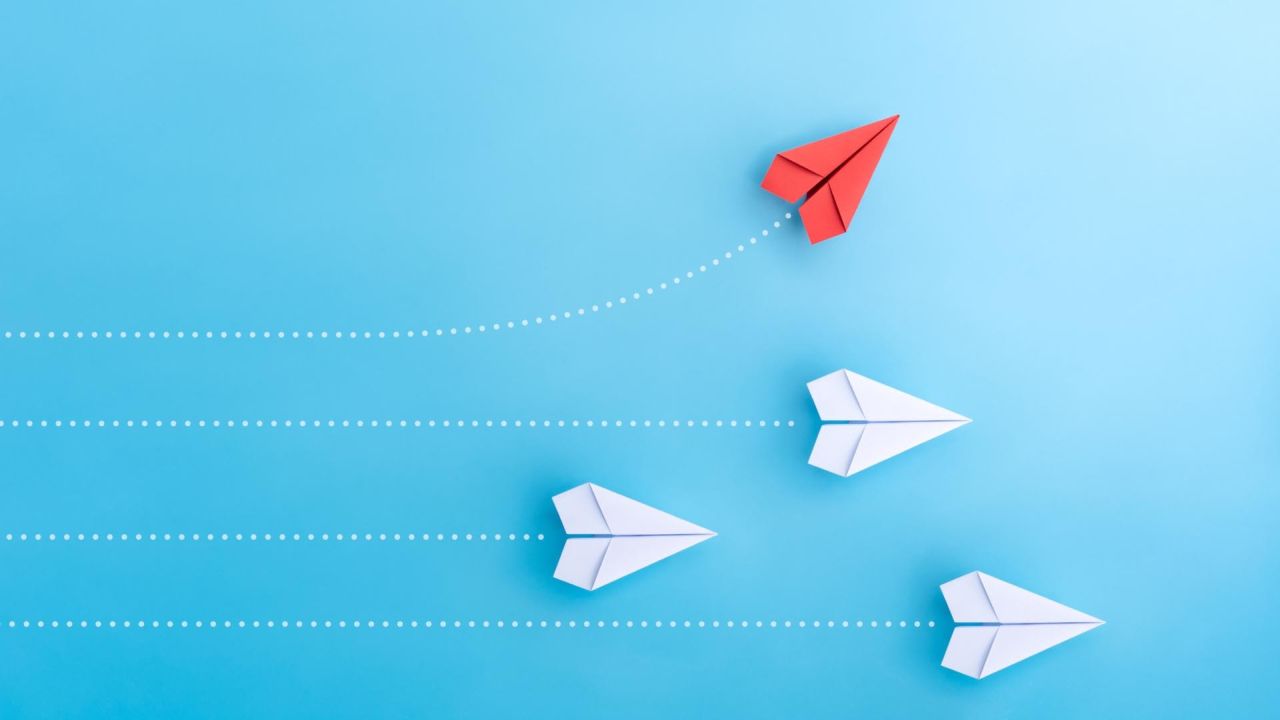 Red paper airplane leading white ones on blue background