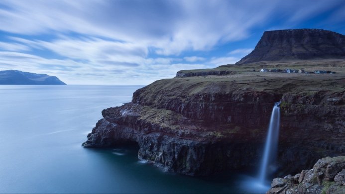 Waterfall flowing into the ocean near a cliffside village in the Faroe Islands