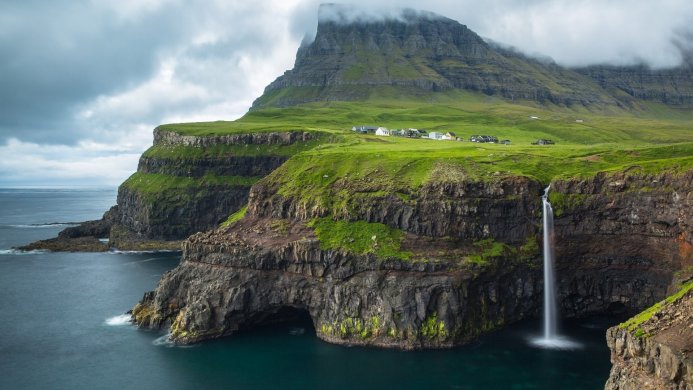 Waterfall flowing from a green cliff into the ocean, with houses on top of the cliff