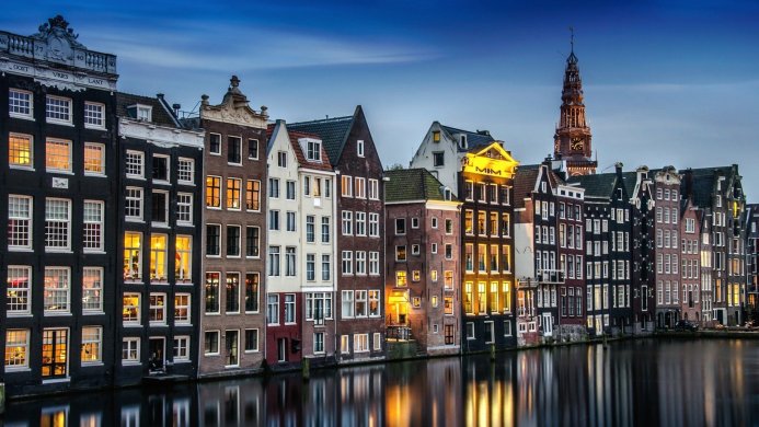 Amsterdam cityscape with canal, houses and a tower under a blue sky