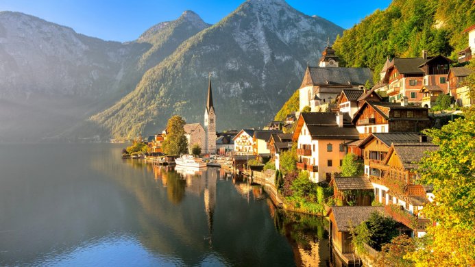 Picturesque village by a lake with mountains in the background. Houses and church reflected in the water