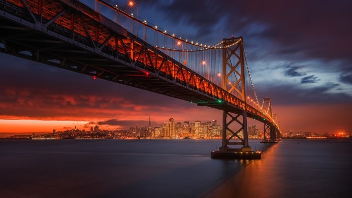 Bay Bridge at night with the city skyline in the background under a cloudy sky