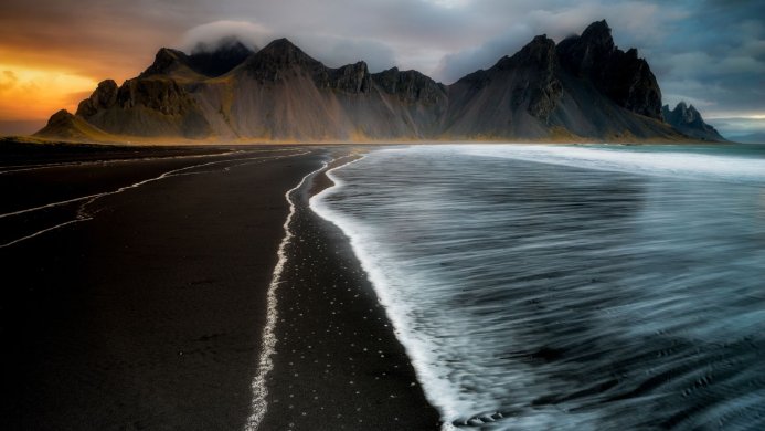 Black sand beach with mountains in Iceland under a cloudy sky