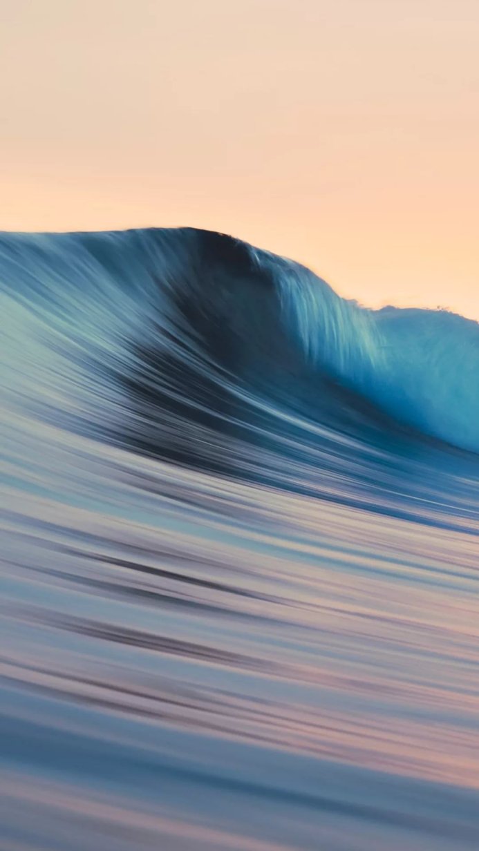 A long exposure image of a large blue ocean wave with an orange sky at sunrise