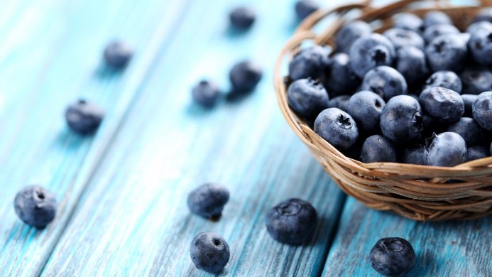 Fresh blueberries in a basket on a blue wooden surface