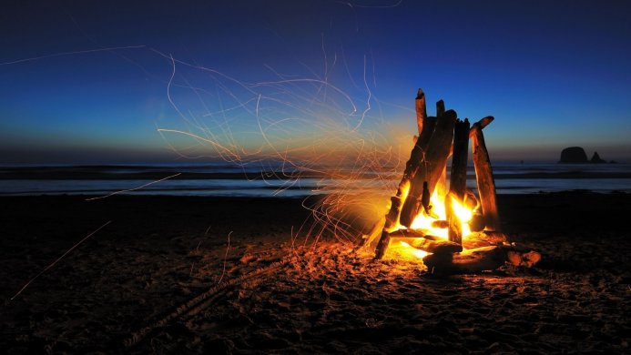 Bonfire on a beach at twilight with sparks flying into the dark blue sky