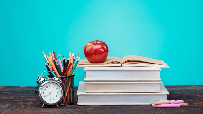 Stack of books with apple, clock, pencils and chalk on a blue background