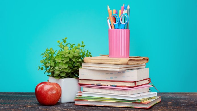 Stack of books, apple, plant, and pencil holder against a teal background