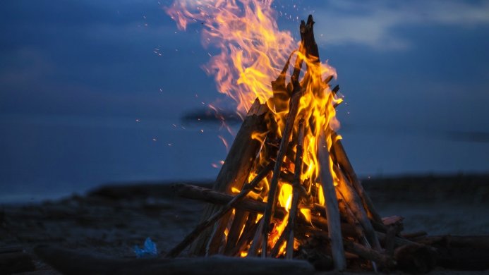 Campfire burning on a beach at night with dark blue sky and glowing embers