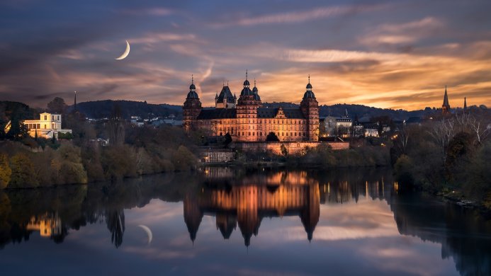 Majestic castle reflecting in the water at dusk under a crescent moon