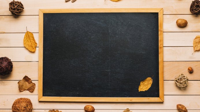 Chalkboard surrounded by leaves, nuts, and wicker balls on a wooden background