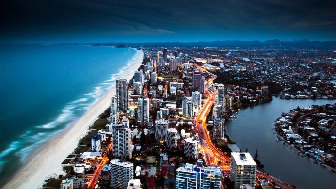 Aerial view of a coastal city at night with bright lights and a long beach