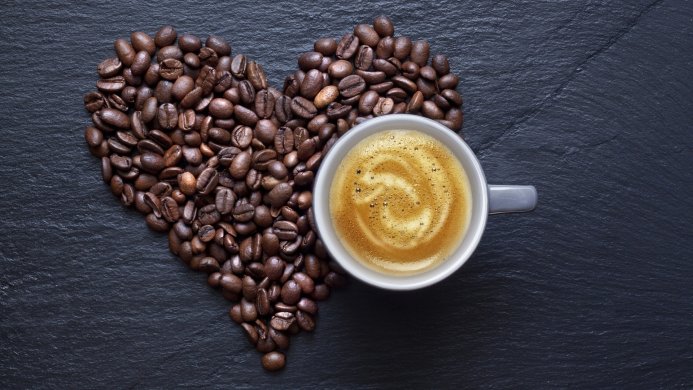 Coffee cup and beans arranged in heart shape on black slate background