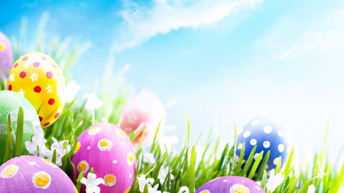 Colorful easter eggs lying on green grass against a blue sky with clouds