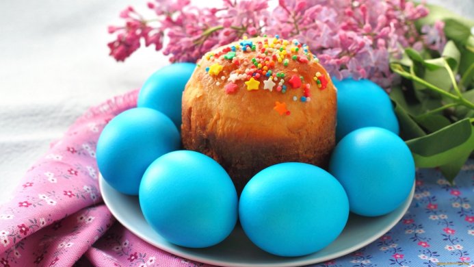 Easter cake decorated with sprinkles, surrounded by blue painted eggs and lilac flowers