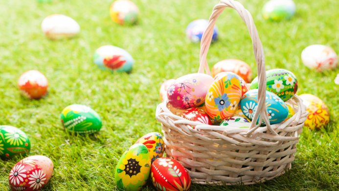 A basket full of decorated Easter eggs sits on a green lawn