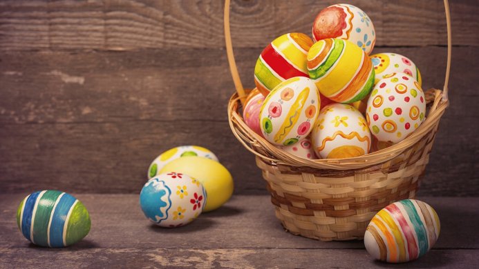 A basket filled with painted Easter eggs on a wooden surface